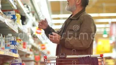 超市里的一位老人正试图在奶制品部门挑选奶酪。 微笑着看着智能手机